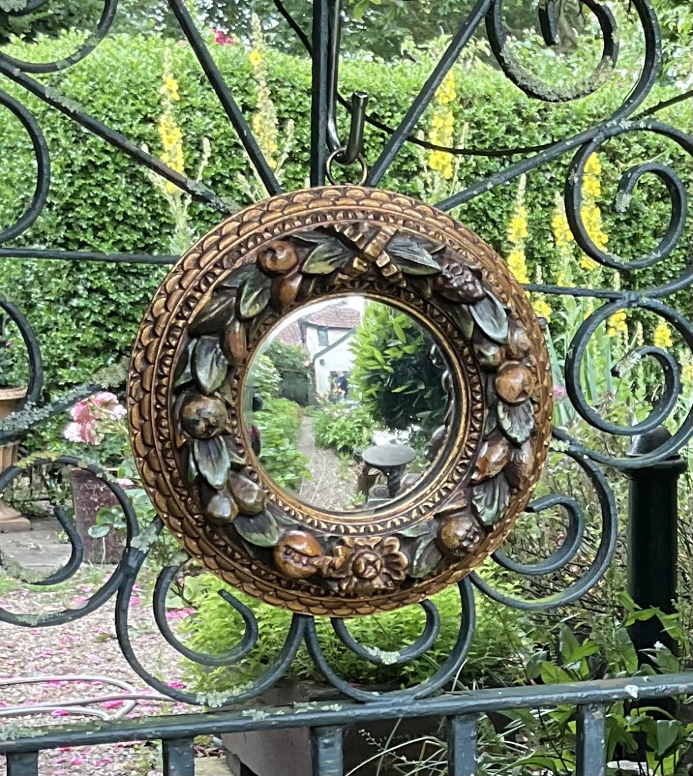 A circular carved wood convex wall mirror featuring a relief fruit and foliage wreath frame with a gilded finish. View II