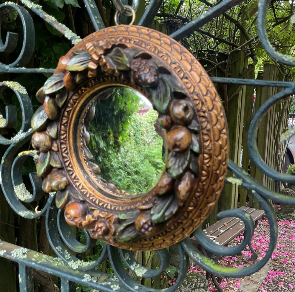 A circular carved wood convex wall mirror featuring a relief fruit and foliage wreath frame with a gilded finish. View III