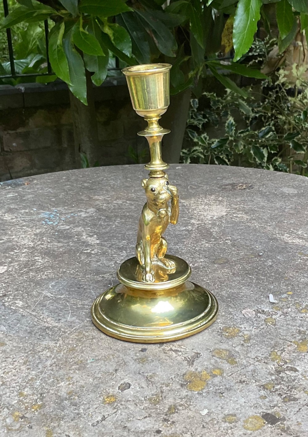 A Victorian cast brass candlestick featuring a sculpted sitting pug dog forming the lower stem above a round stepped base. View III