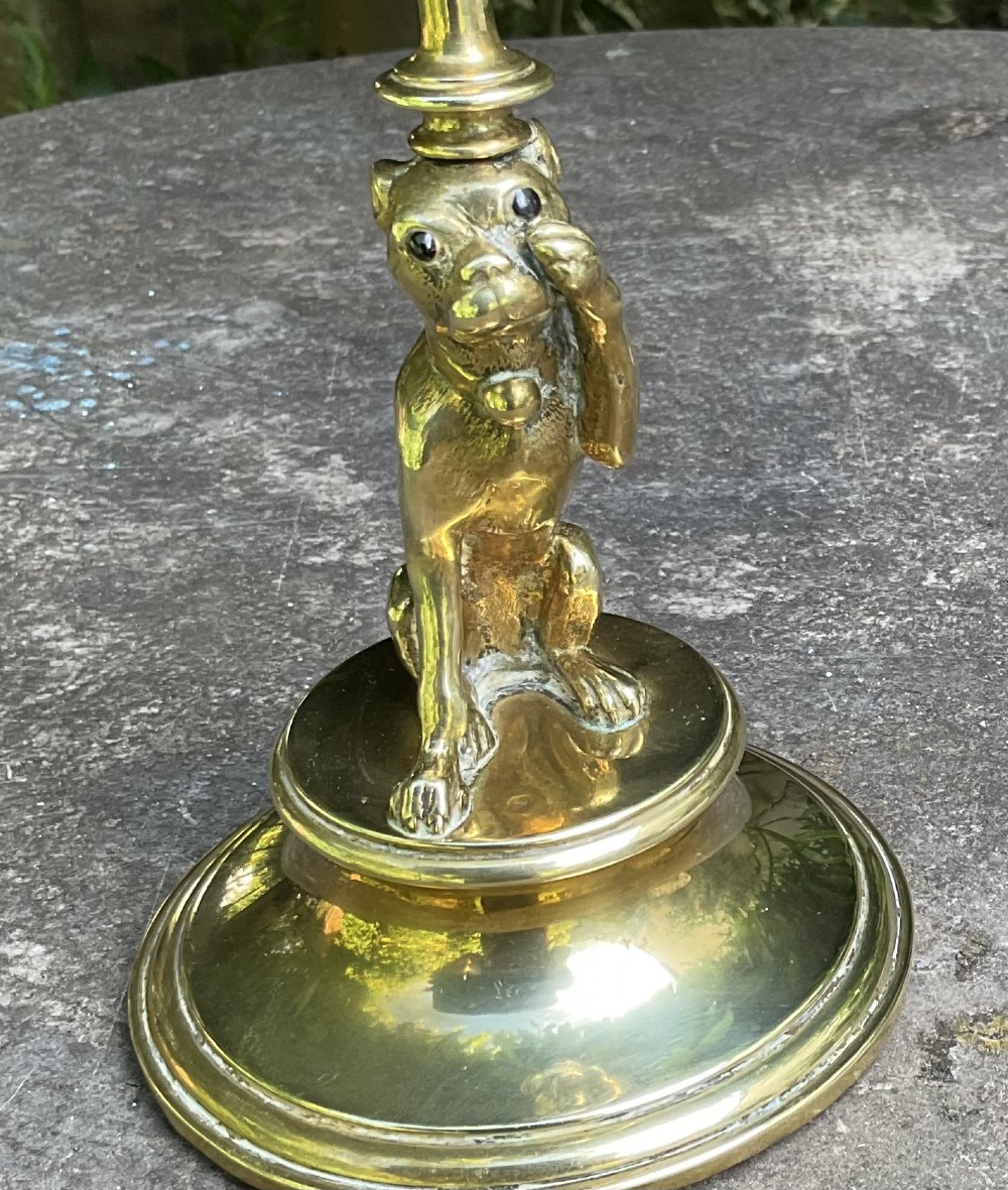 A Victorian cast brass candlestick featuring a sculpted sitting pug dog forming the lower stem above a round stepped base. View VIII