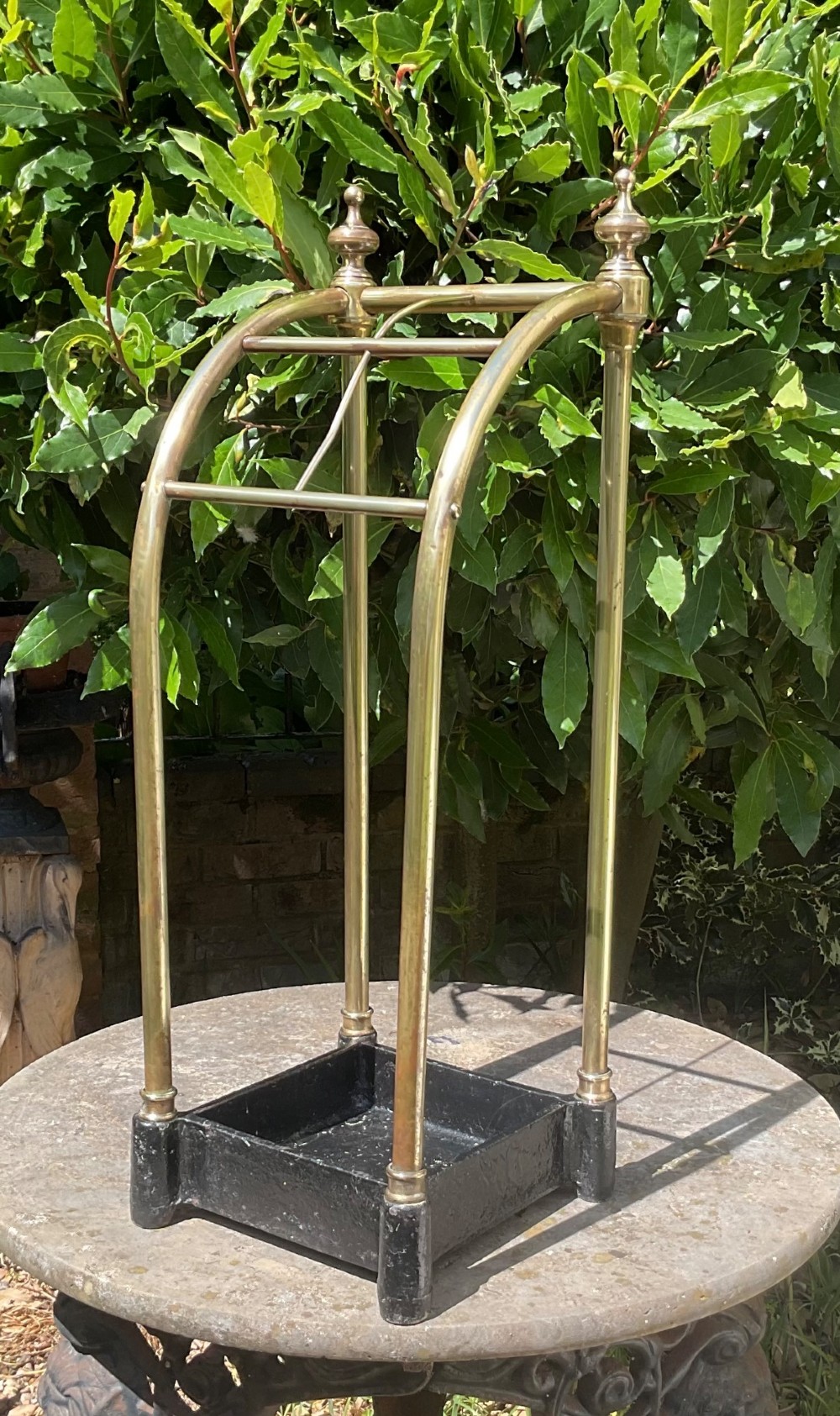 An Edwardian brass umbrella stand featuring tubular metal arches, decorative top finials, and a heavy black cast iron drip tray base.
