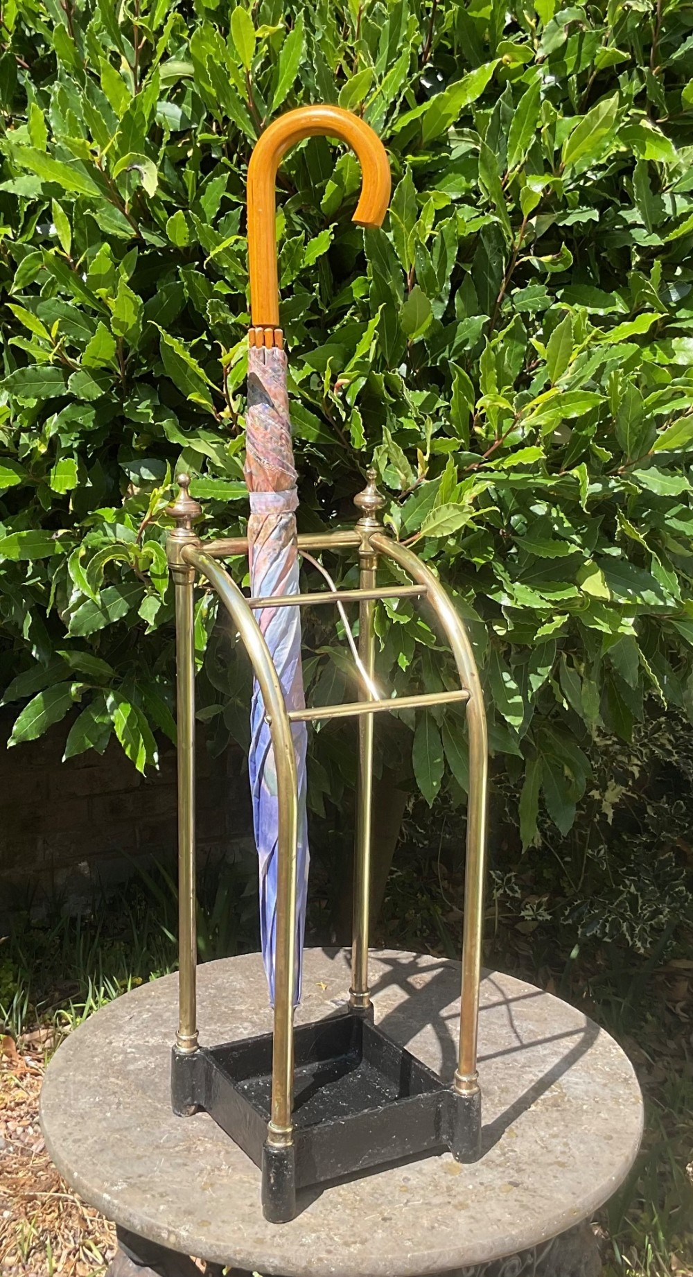 An Edwardian brass umbrella stand featuring tubular metal arches, decorative top finials, and a heavy black cast iron drip tray base. View II