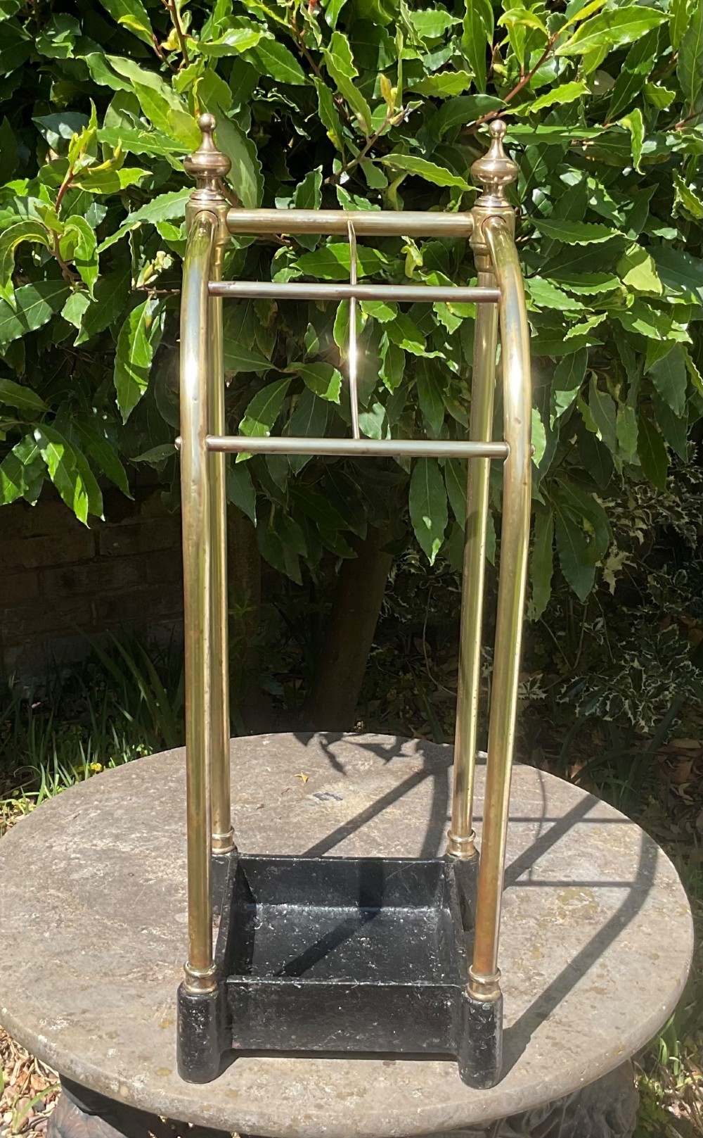 An Edwardian brass umbrella stand featuring tubular metal arches, decorative top finials, and a heavy black cast iron drip tray base. View III