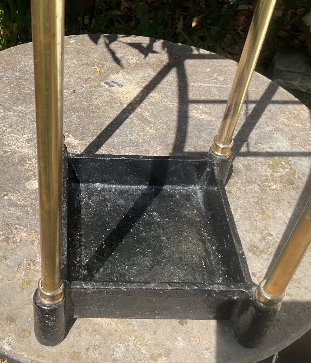 An Edwardian brass umbrella stand featuring tubular metal arches, decorative top finials, and a heavy black cast iron drip tray base. View IV