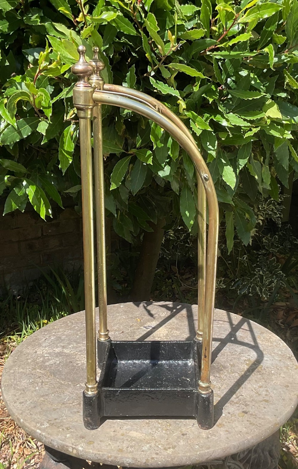 An Edwardian brass umbrella stand featuring tubular metal arches, decorative top finials, and a heavy black cast iron drip tray base. View V