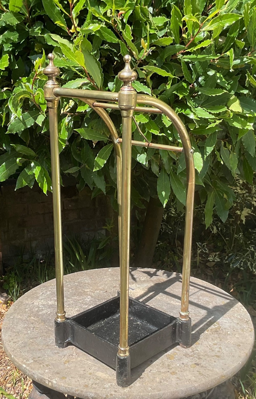 An Edwardian brass umbrella stand featuring tubular metal arches, decorative top finials, and a heavy black cast iron drip tray base. View VI