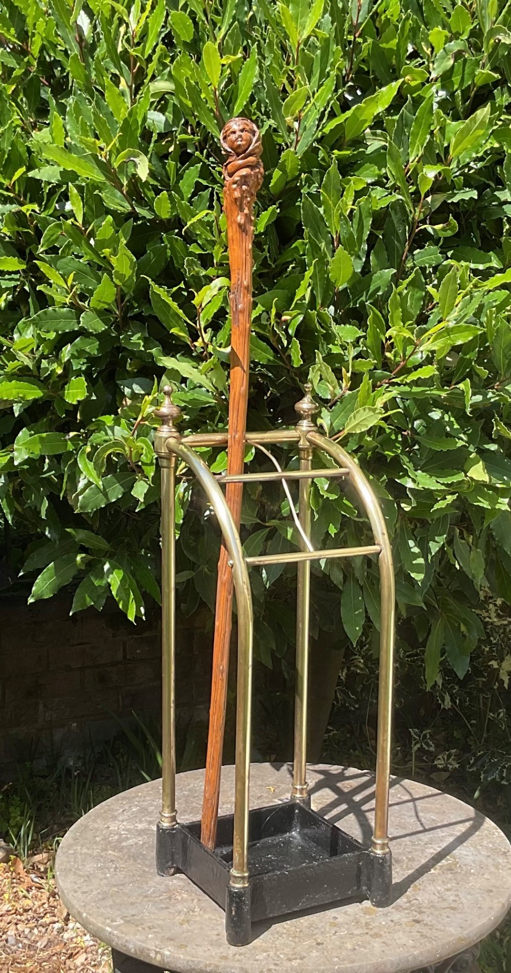 An Edwardian brass umbrella stand featuring tubular metal arches, decorative top finials, and a heavy black cast iron drip tray base. View VII