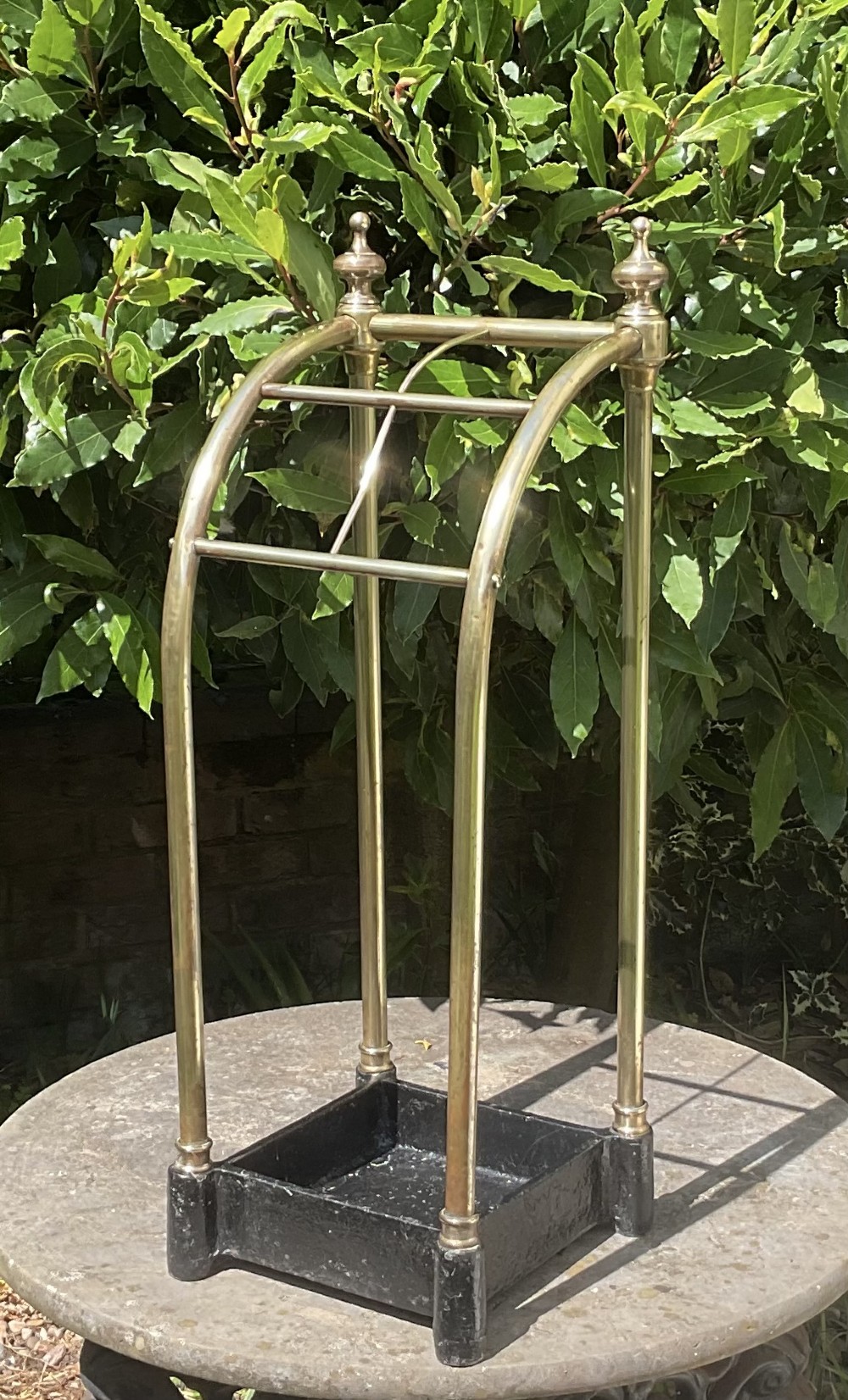 An Edwardian brass umbrella stand featuring tubular metal arches, decorative top finials, and a heavy black cast iron drip tray base. View VIII