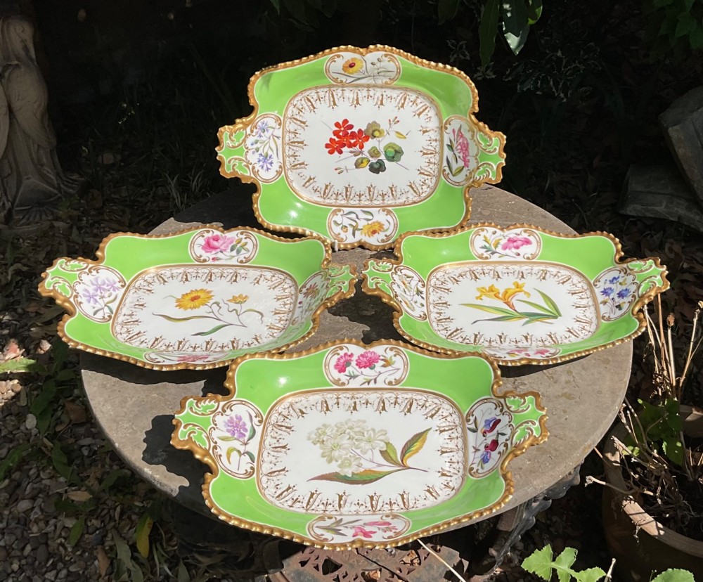 A set of four Regency period Chamberlains Worcester porcelain serving dishes featuring bright apple green borders, gilt scrollwork, and individual hand-painted central botanical flowers.