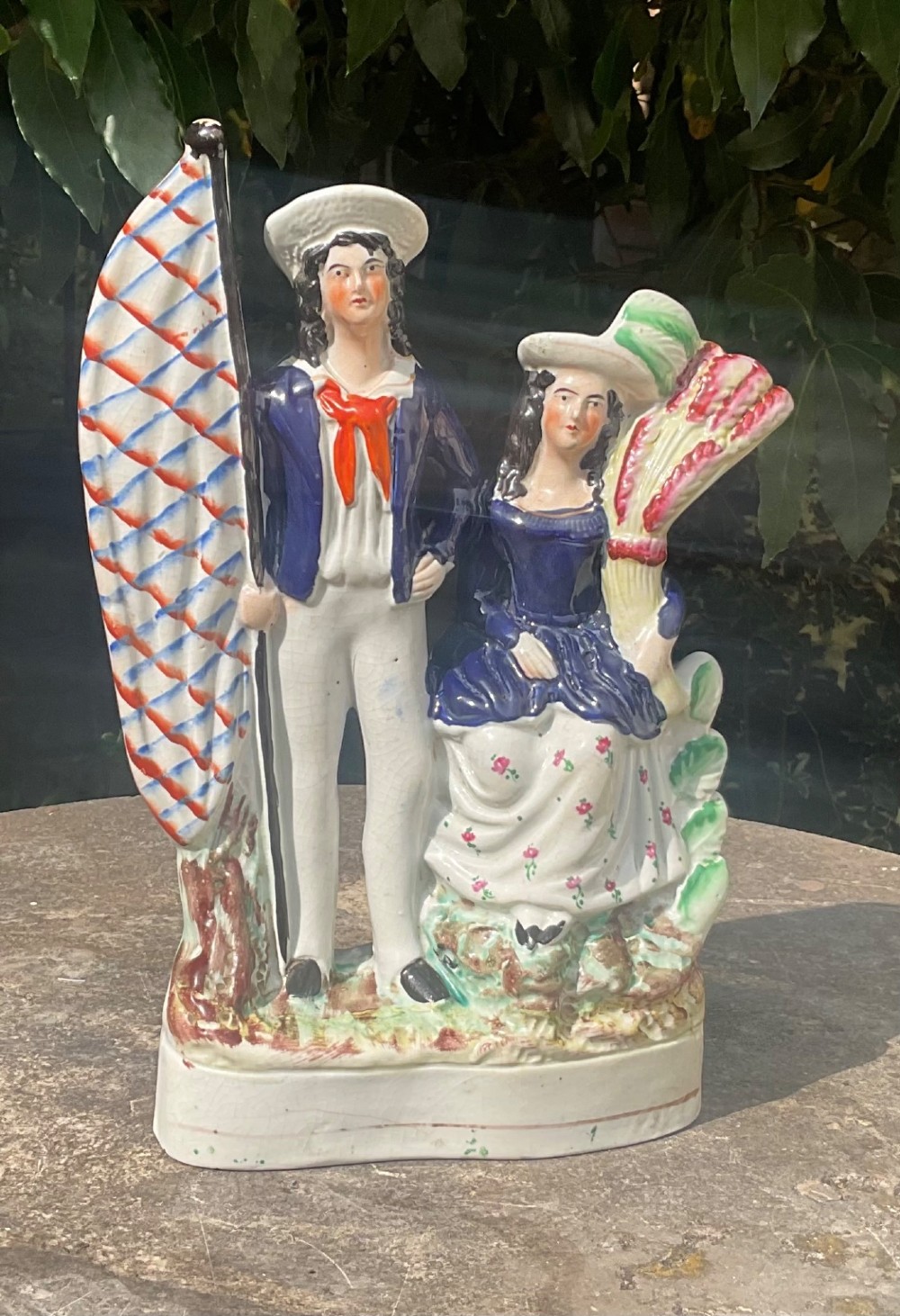 A Victorian Staffordshire earthenware flatback figure group depicting a sailor holding a flag alongside a female figure holding a sheaf of corn.