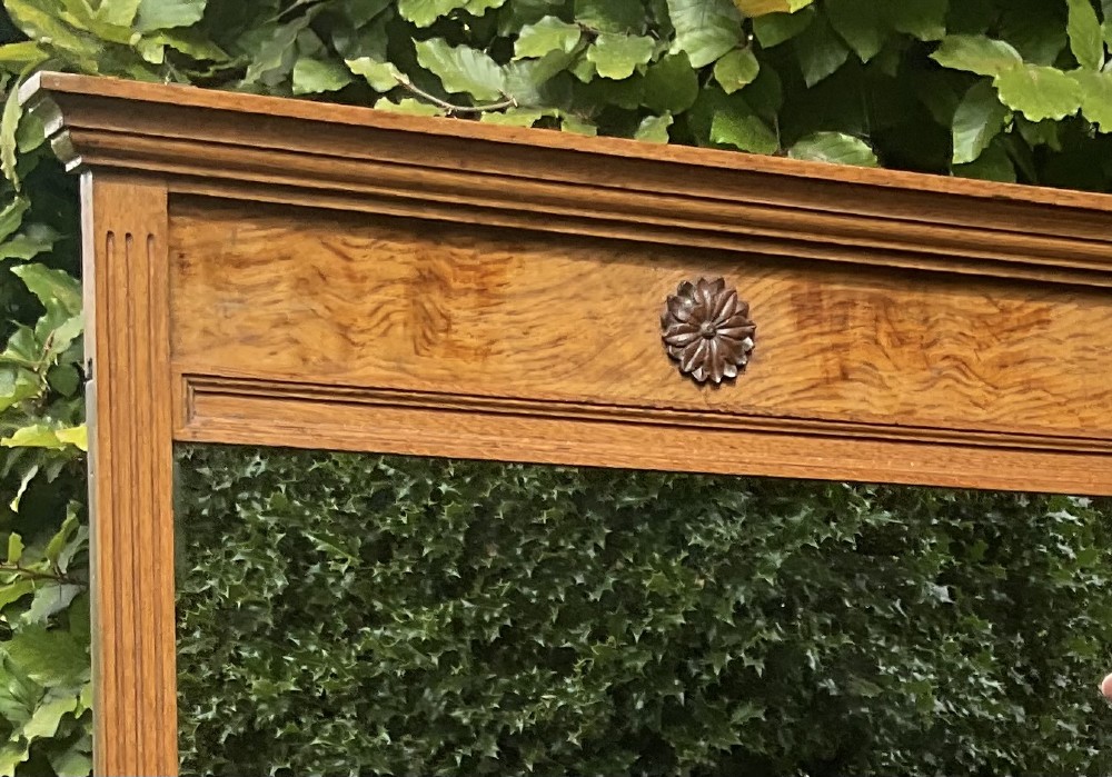 A rectangular Edwardian blonde oak mirror featuring a moulded cornice top, central carved rosette motif, fluted side pilasters, and a clear glass plate. View II