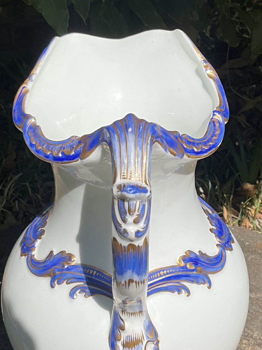 A 19th-century white porcelain water jug featuring cobalt blue foliage mouldings highlighted with gold leaf detailing along the rim, handle, shoulder, and base. View V