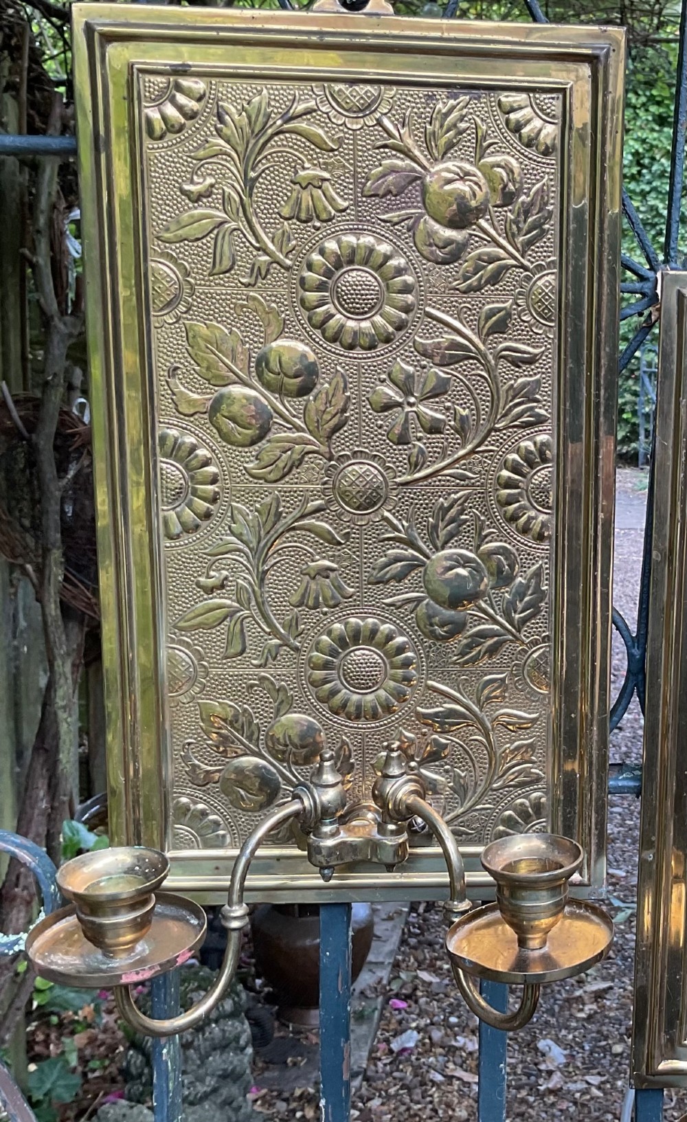 A pair of rectangular brass wall sconces featuring embossed sunflower and floral relief panels with twin candle branches attached near the base. View II