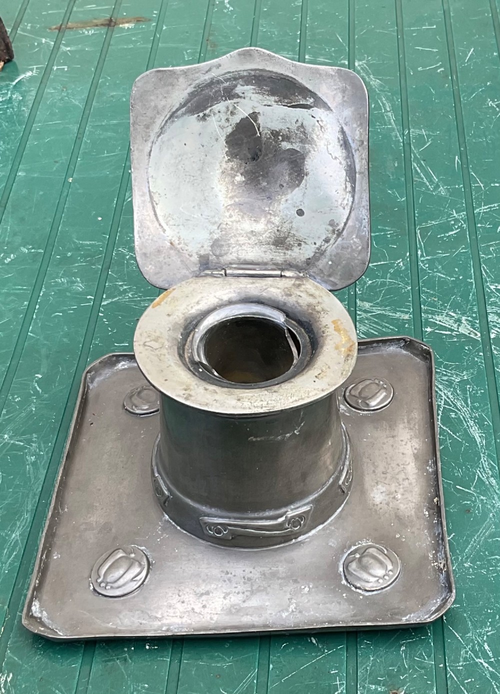An Arts and Crafts Tudric pewter inkwell featuring a square base tray with raised relief motifs and a central cylindrical body topped with a square lid. View III