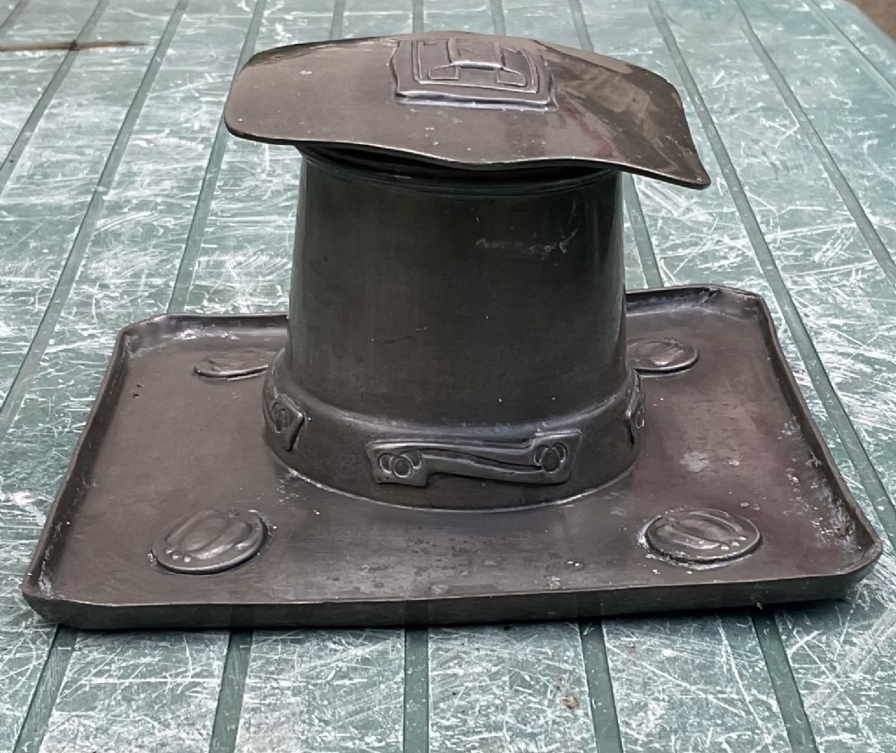An Arts and Crafts Tudric pewter inkwell featuring a square base tray with raised relief motifs and a central cylindrical body topped with a square lid. View VIII