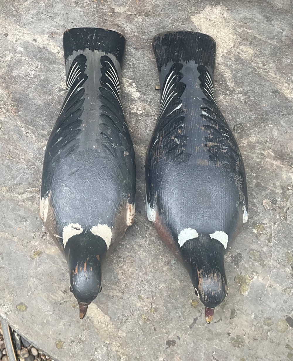 A pair of hand-carved, painted wooden wood pigeon decoys with weathered grey, black, and white plumage. View II