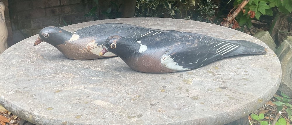 A pair of hand-carved, painted wooden wood pigeon decoys with weathered grey, black, and white plumage. View V
