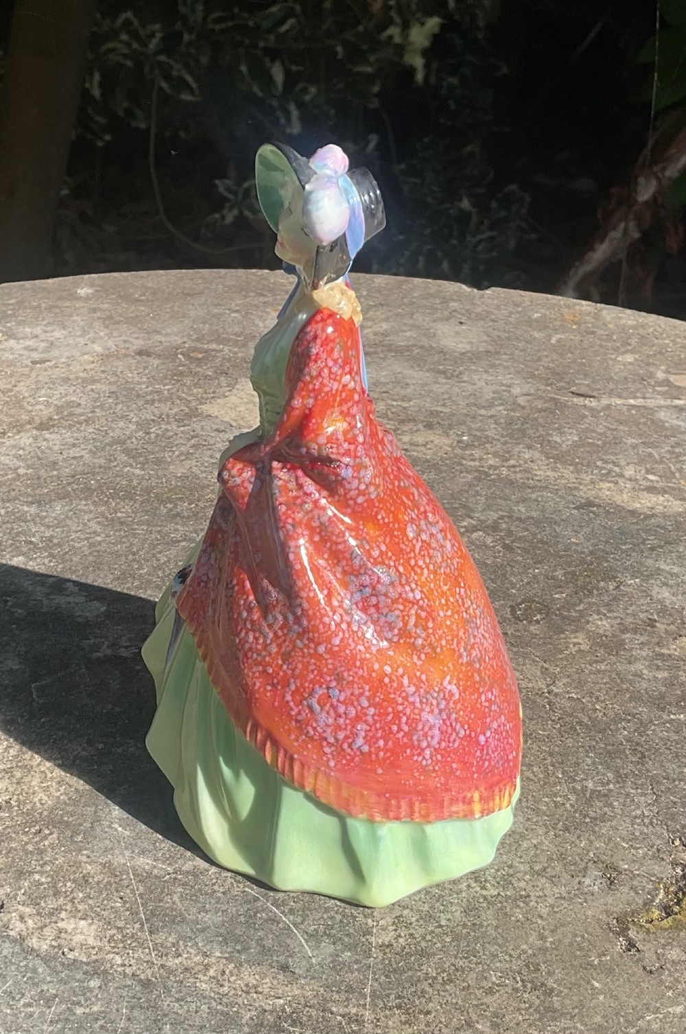 A Royal Doulton fine bone china figurine depicting a woman in a green gown and bonnet holding a parasol and draped in a patterned red shawl. View II