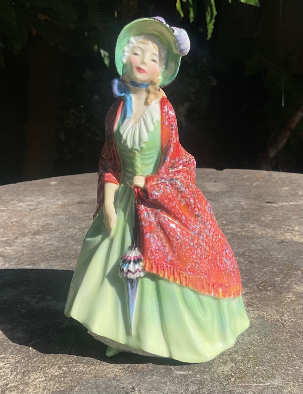A Royal Doulton fine bone china figurine depicting a woman in a green gown and bonnet holding a parasol and draped in a patterned red shawl. View VI