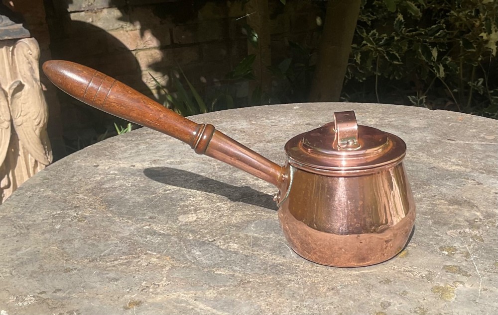 An 1830s Georgian copper brandy warmer featuring a polished copper vessel, fitted lid with loop handle, pouring spout, and an extended turned wooden handle. View IV
