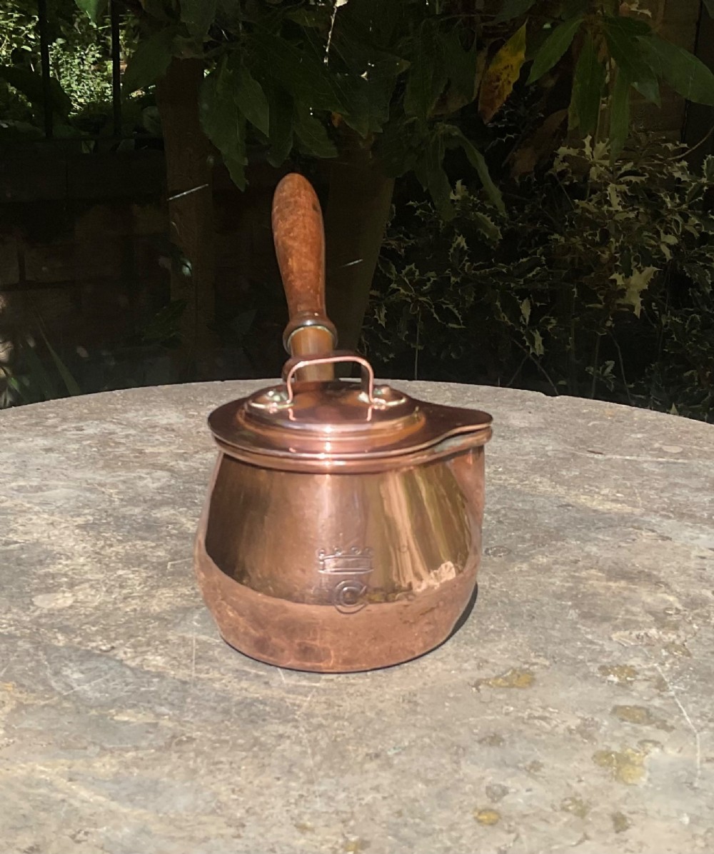 An 1830s Georgian copper brandy warmer featuring a polished copper vessel, fitted lid with loop handle, pouring spout, and an extended turned wooden handle. View V
