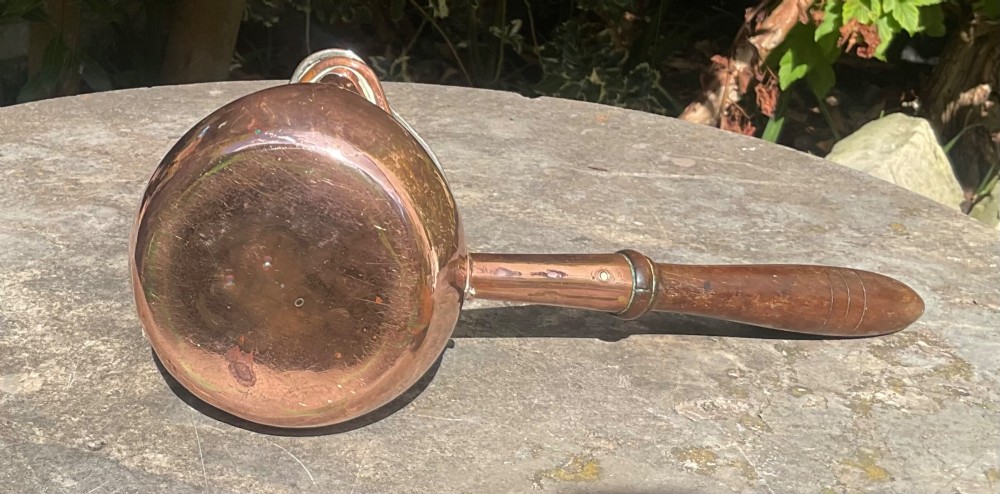 An 1830s Georgian copper brandy warmer featuring a polished copper vessel, fitted lid with loop handle, pouring spout, and an extended turned wooden handle. View VI