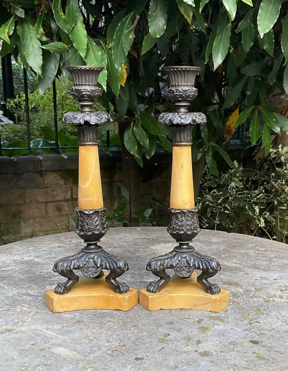 A pair of Regency period candlesticks with yellow marble column stems, classical dark bronze sconces, acanthus collars, and bronze paw feet on triform marble bases. View II