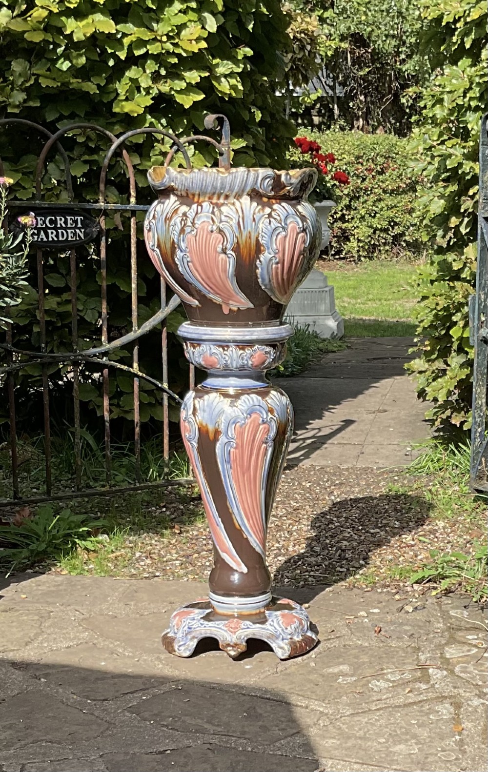 A late Victorian glazed majolica ceramic jardiniere resting atop a matching relief-moulded pedestal stand with brown, blue, and pink glazes.