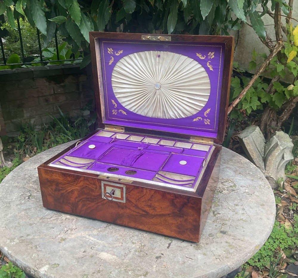 An open Victorian walnut sewing box featuring a fitted purple silk interior and a pleated cream silk panel on the inside lid.