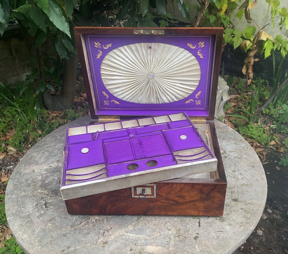 An open Victorian walnut sewing box featuring a fitted purple silk interior and a pleated cream silk panel on the inside lid. View II