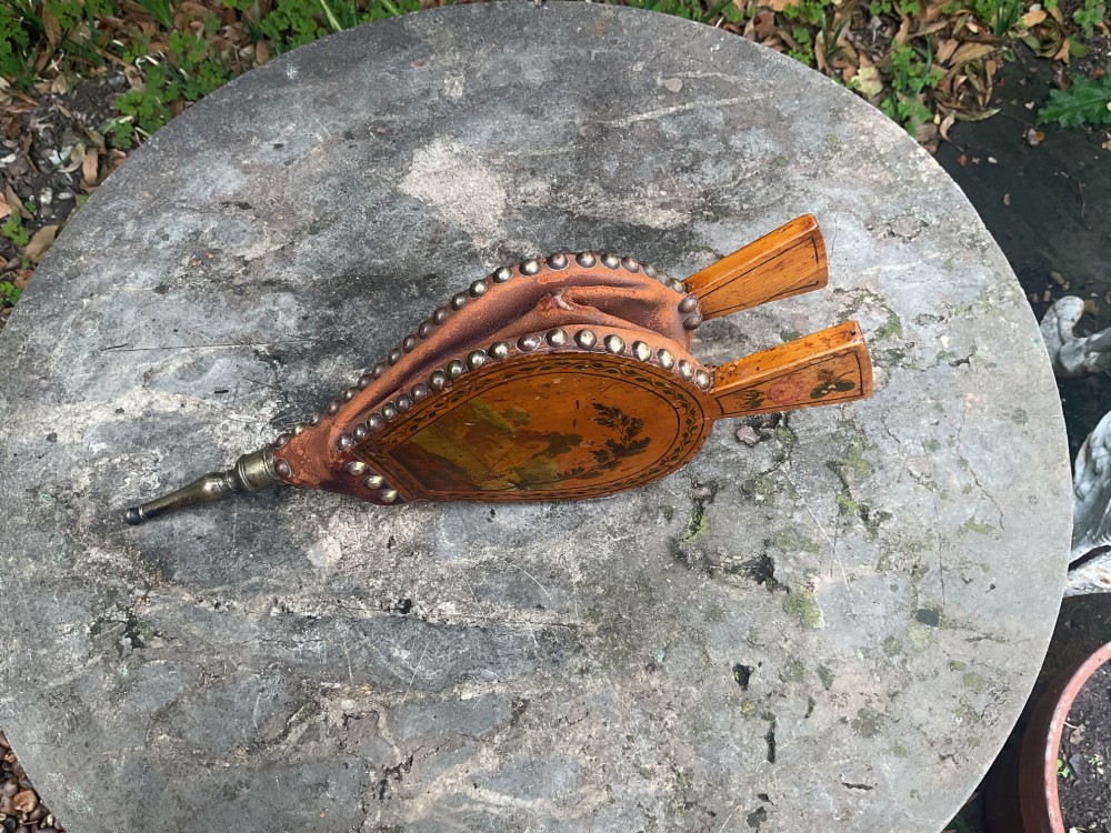 A Regency-period hand-painted wooden fire bellows featuring a painted landscape scene, brass nozzle, tan leather sides, and decorative brass studs. View VI