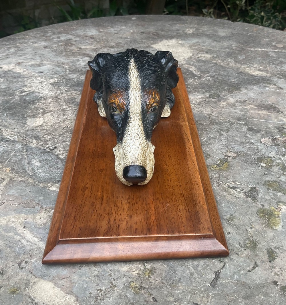 A cold-painted bronze dogs head mounted as a spring-loaded letter clip on a rectangular polished wooden plinth. View II