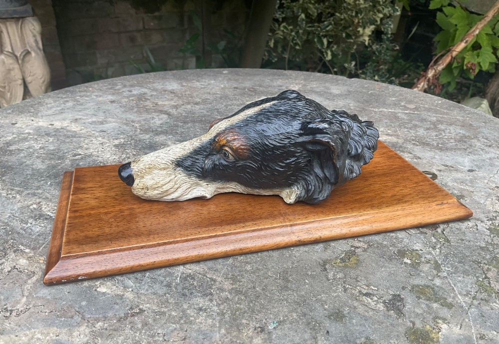 A cold-painted bronze dogs head mounted as a spring-loaded letter clip on a rectangular polished wooden plinth. View III