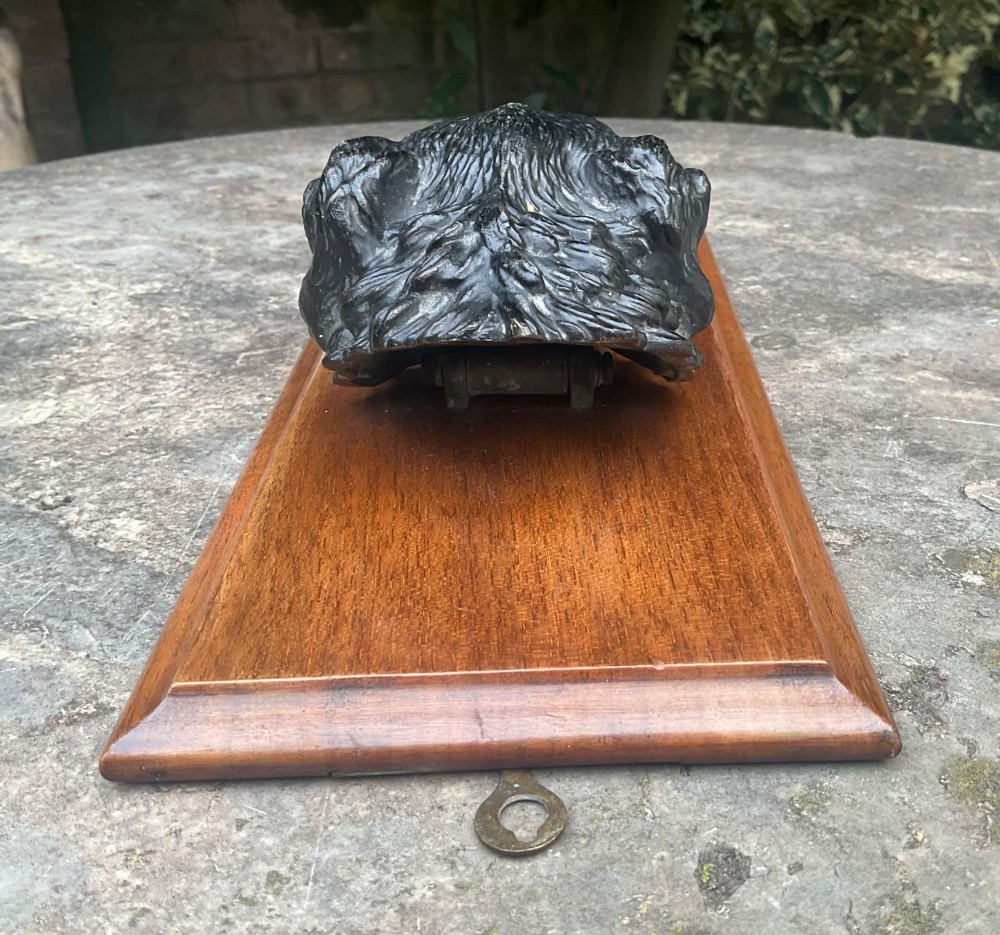 A cold-painted bronze dogs head mounted as a spring-loaded letter clip on a rectangular polished wooden plinth. View IV