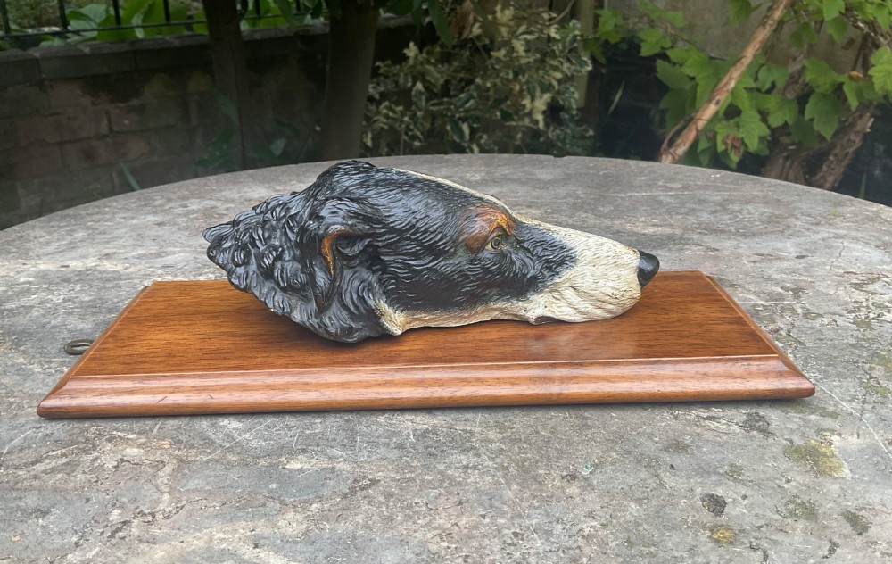 A cold-painted bronze dogs head mounted as a spring-loaded letter clip on a rectangular polished wooden plinth. View VI