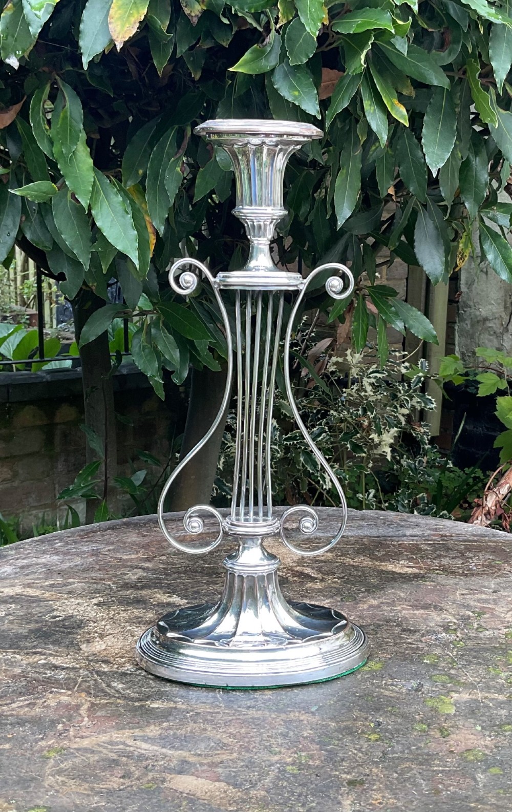 A tall silver-plated candlestick designed in the Adam style featuring a lyre-shaped central column, scroll motifs, and a fluted sconce over a circular moulded base.