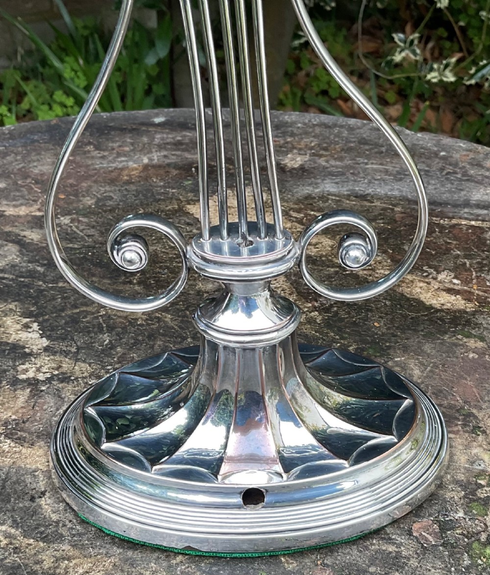 A tall silver-plated candlestick designed in the Adam style featuring a lyre-shaped central column, scroll motifs, and a fluted sconce over a circular moulded base. View IV