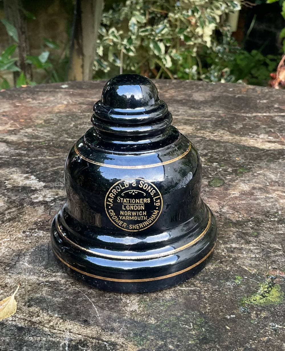 A domed black glazed pottery inkwell decorated with gilded concentric bands and transfer-printed lettering reading Jarrold and Sons Stationers.