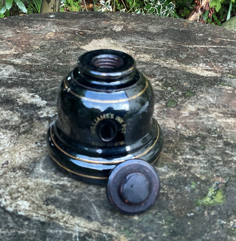 A domed black glazed pottery inkwell decorated with gilded concentric bands and transfer-printed lettering reading Jarrold and Sons Stationers. View III