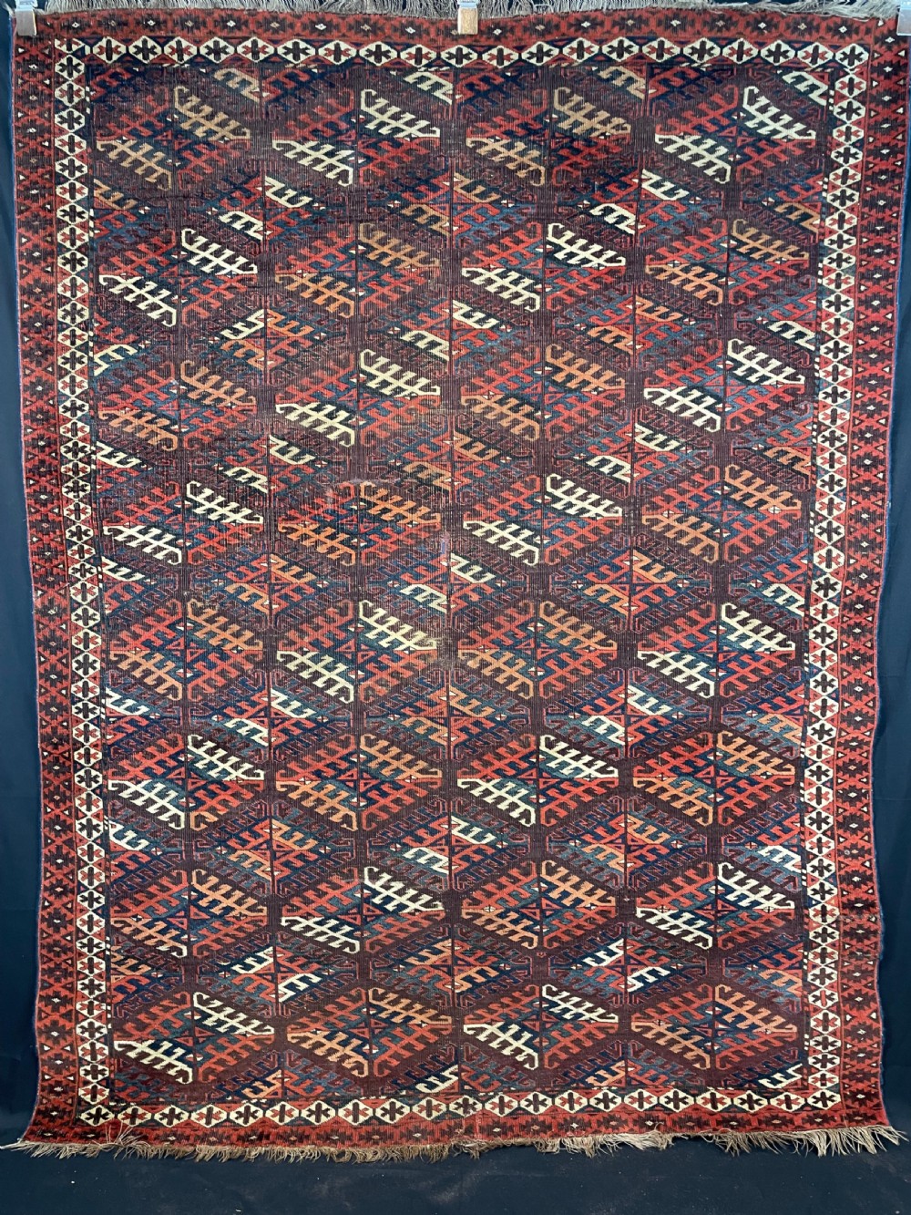 An antique Yomut Turkoman hand-knotted wool rug featuring repeating geometric diamond lattice motifs in deep red, navy blue, and ivory shades.