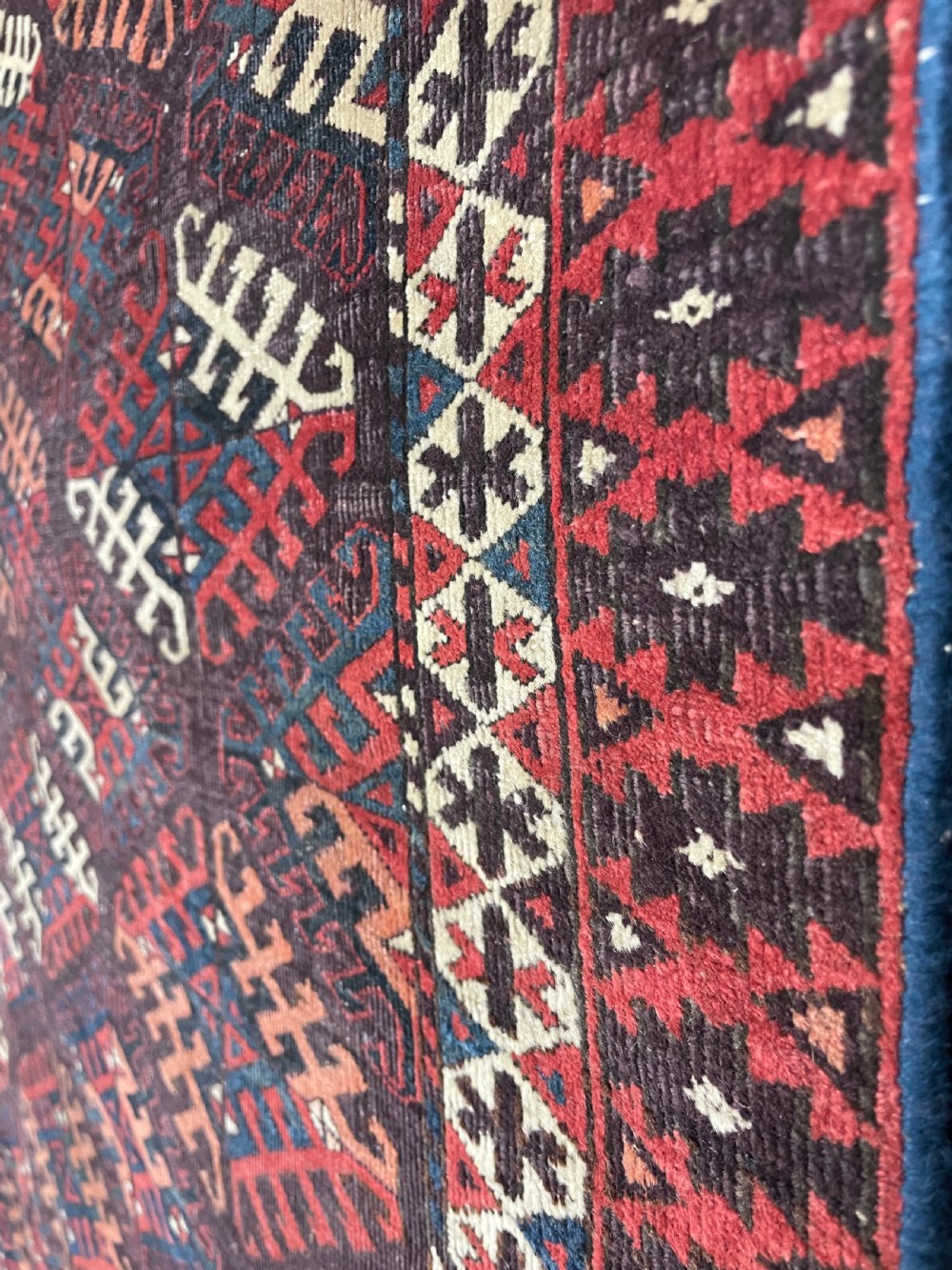 An antique Yomut Turkoman hand-knotted wool rug featuring repeating geometric diamond lattice motifs in deep red, navy blue, and ivory shades. View IV
