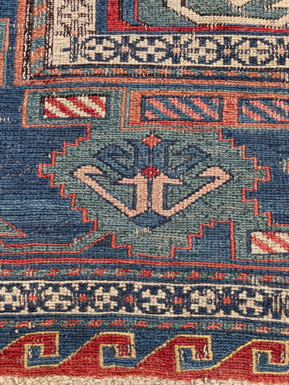 An antique Caucasian Dragon Soumak flatweave wool rug featuring geometric diamond medallions and dragon motifs in terracotta red, navy blue, and teal green. View X