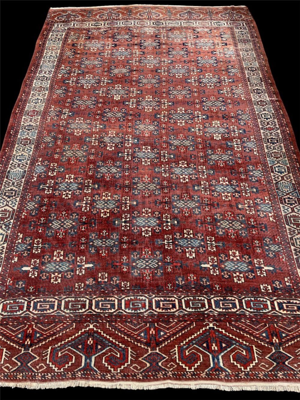A large antique hand-knotted wool Turkoman Yomut carpet featuring repeating geometric gol motifs on a deep red ground surrounded by geometric borders. View III
