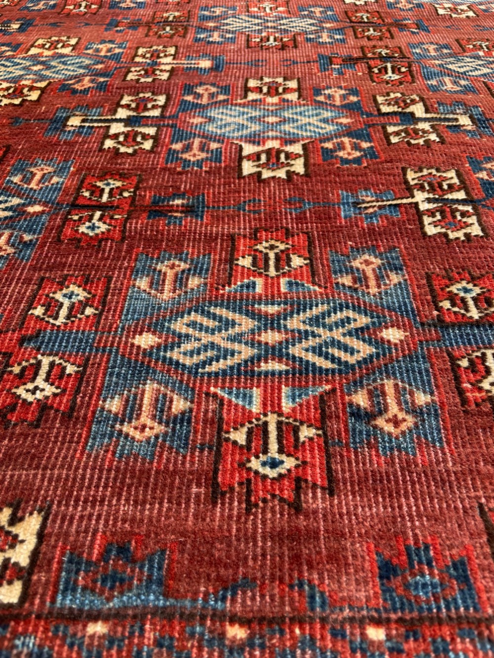 A large antique hand-knotted wool Turkoman Yomut carpet featuring repeating geometric gol motifs on a deep red ground surrounded by geometric borders. View IV