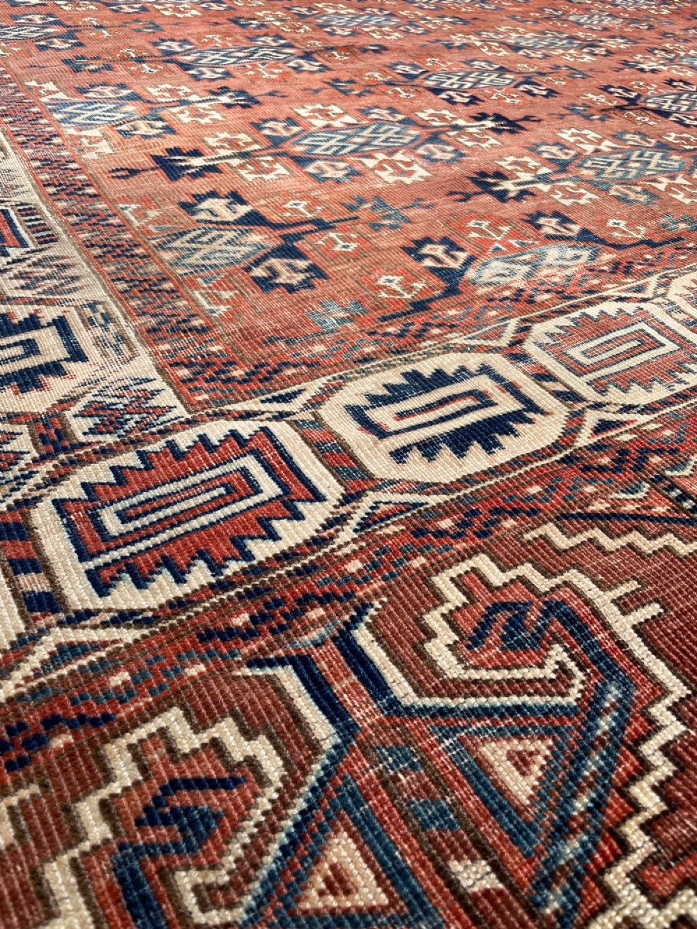A large antique hand-knotted wool Turkoman Yomut carpet featuring repeating geometric gol motifs on a deep red ground surrounded by geometric borders. View X