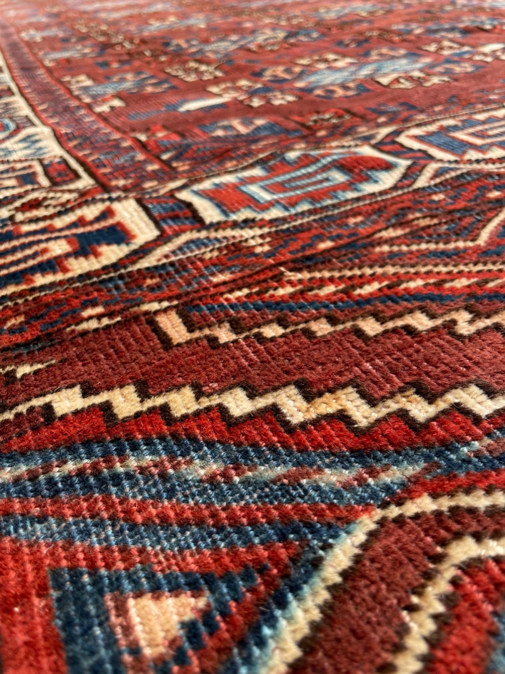 A large antique hand-knotted wool Turkoman Yomut carpet featuring repeating geometric gol motifs on a deep red ground surrounded by geometric borders. View XI