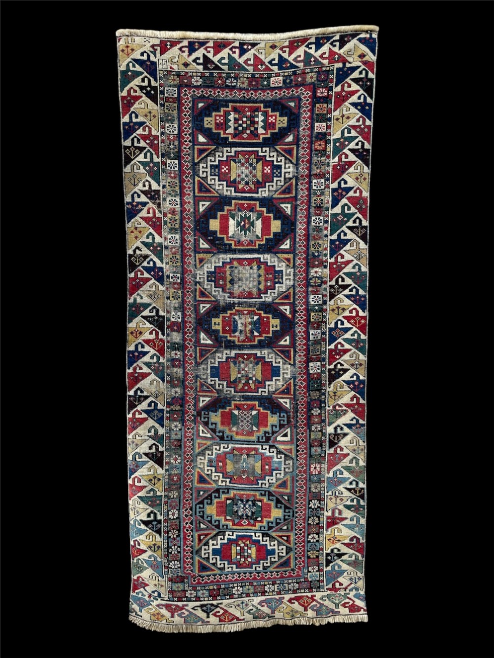 A long hand-knotted wool Shirvan runner rug featuring a central row of geometric stepped medallions framed by detailed multi-coloured bird and hook borders.