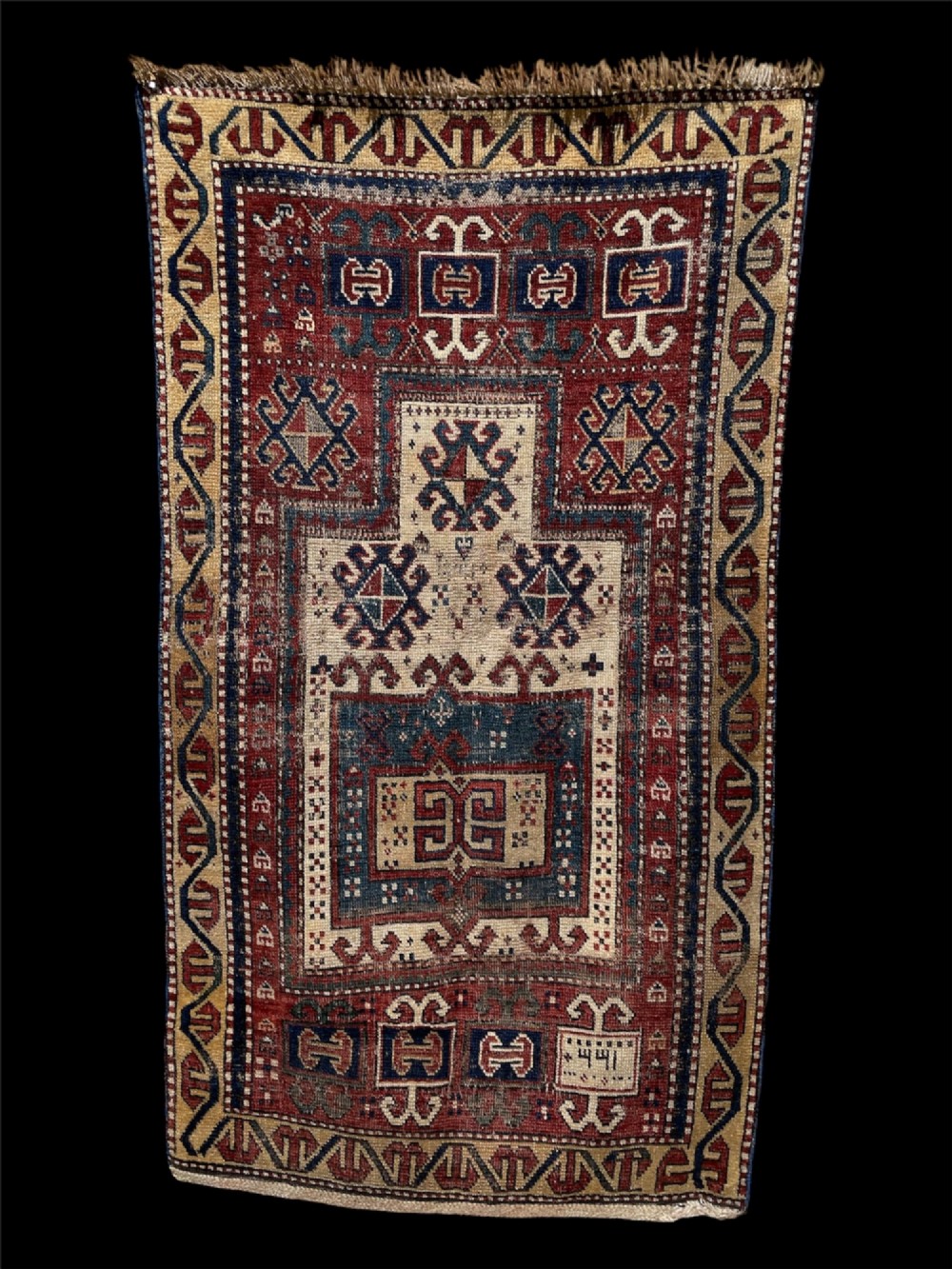 An antique Caucasian Fachralo wool prayer rug featuring a central red field, an ivory geometric mihrab arch, and traditional patterned borders.