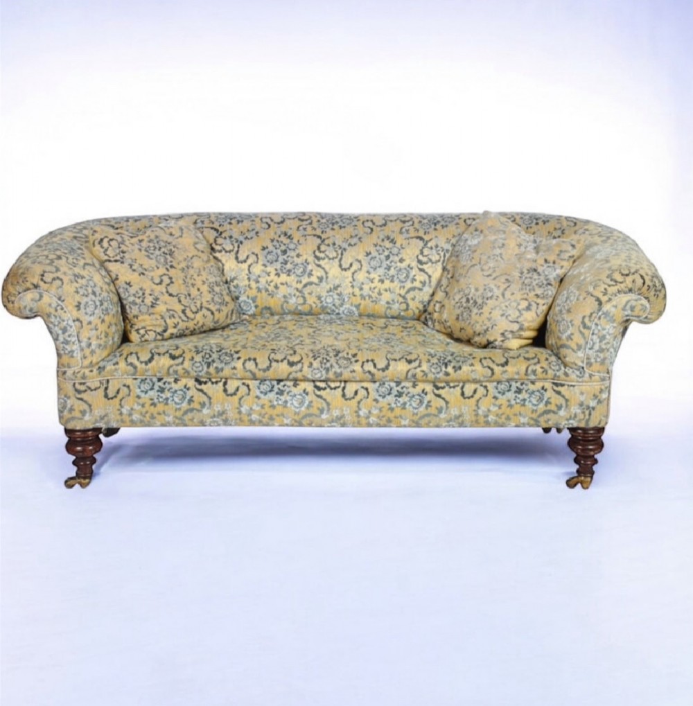 A 19th-century Victorian Chesterfield sofa upholstered in yellow floral patterned fabric with rolled arms and turned wooden legs on castors.