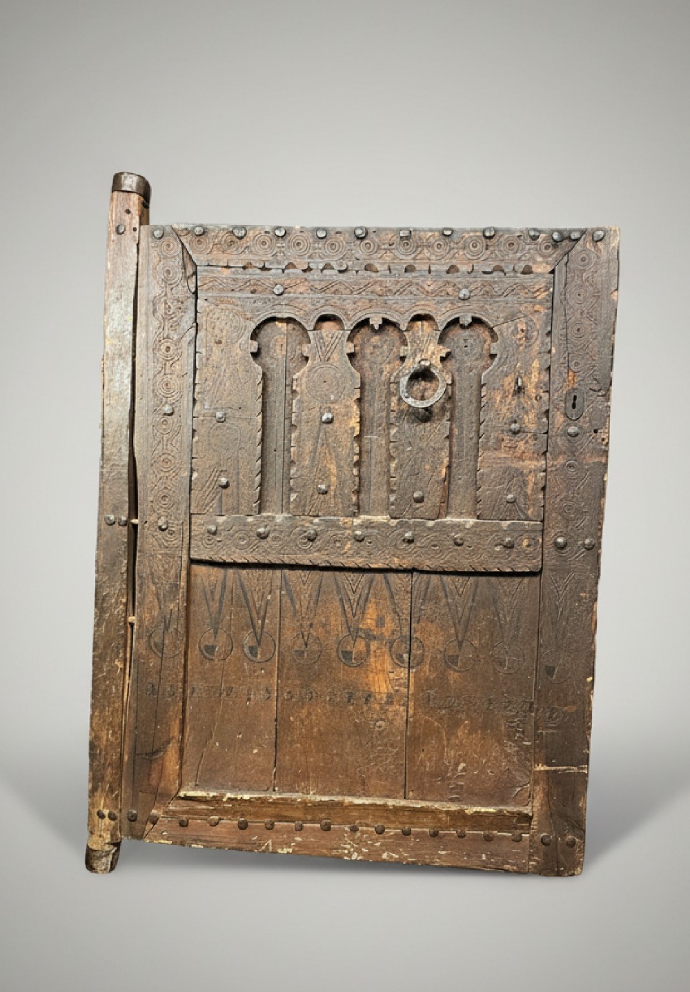 A hand-carved dark timber Amazigh door featuring geometric relief patterns, wrought iron studs, and a circular iron knocker.